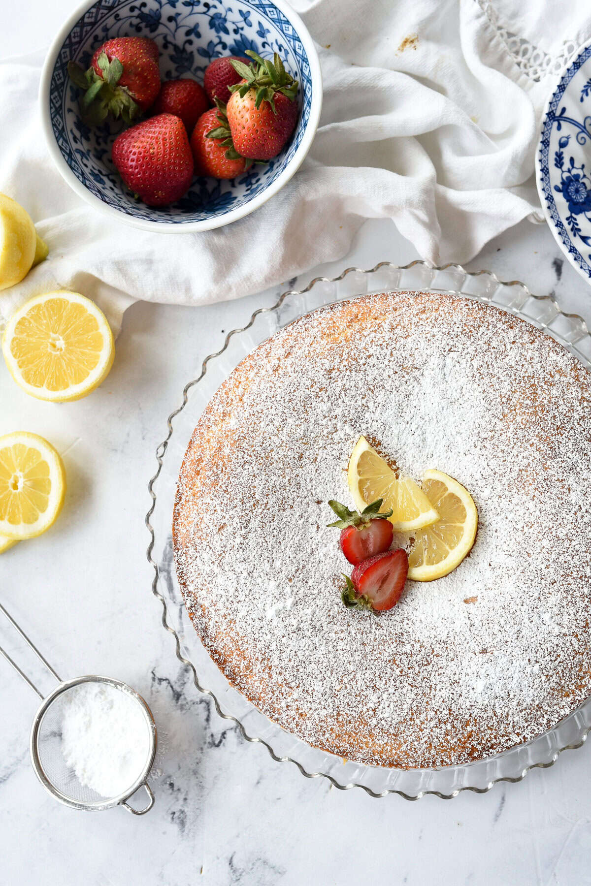 Lemon ricotta cake on a plate with lemons and strawberries on top